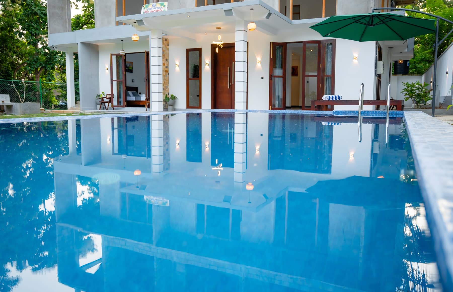 The pool seen along its length, with the villa terrace and a green parasol at the far end
