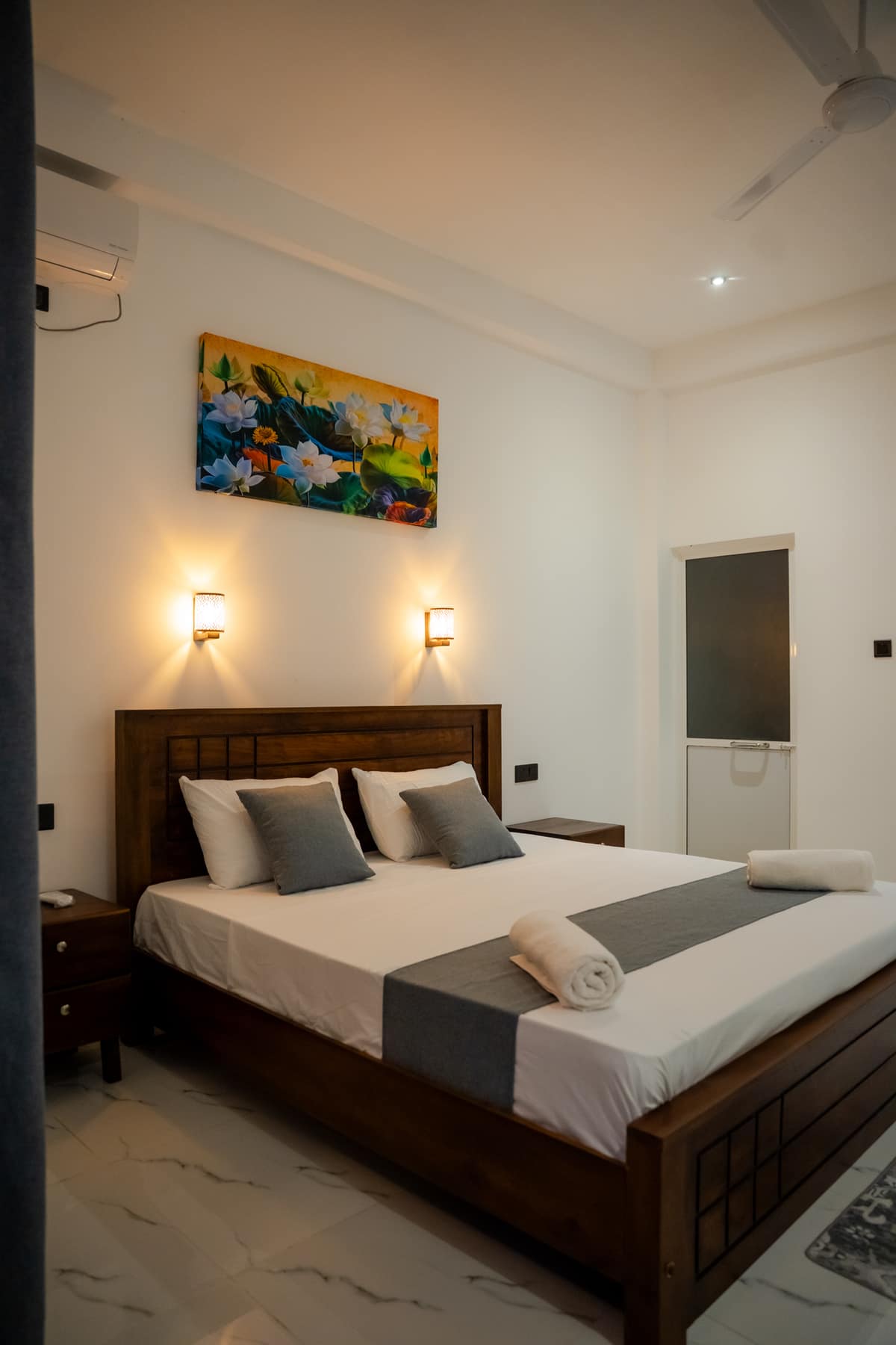 The Deluxe King Room from the doorway — king bed, air-conditioning unit, a reading light on either side of the headboard