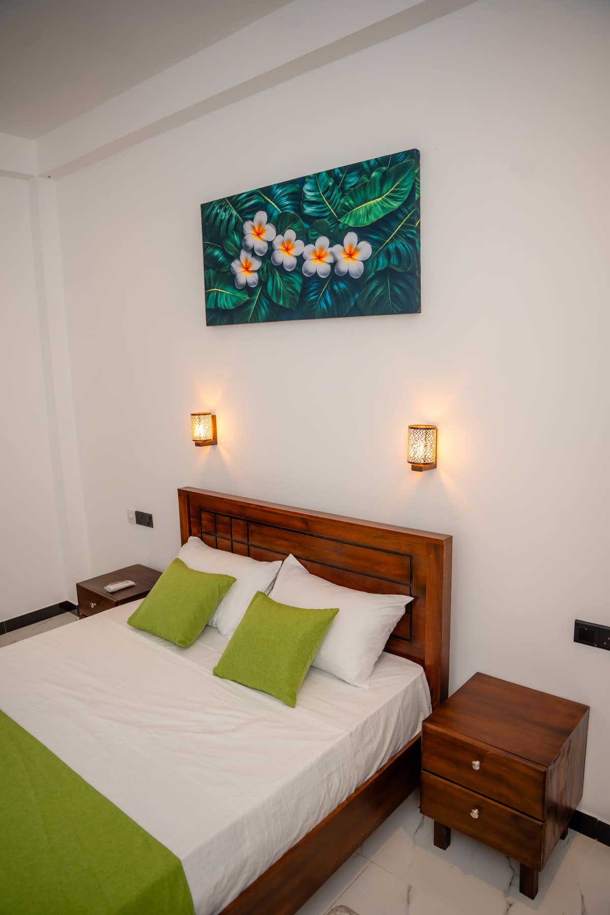 The Deluxe Queen Room seen from the foot of the bed, with the bedside table and wall lights