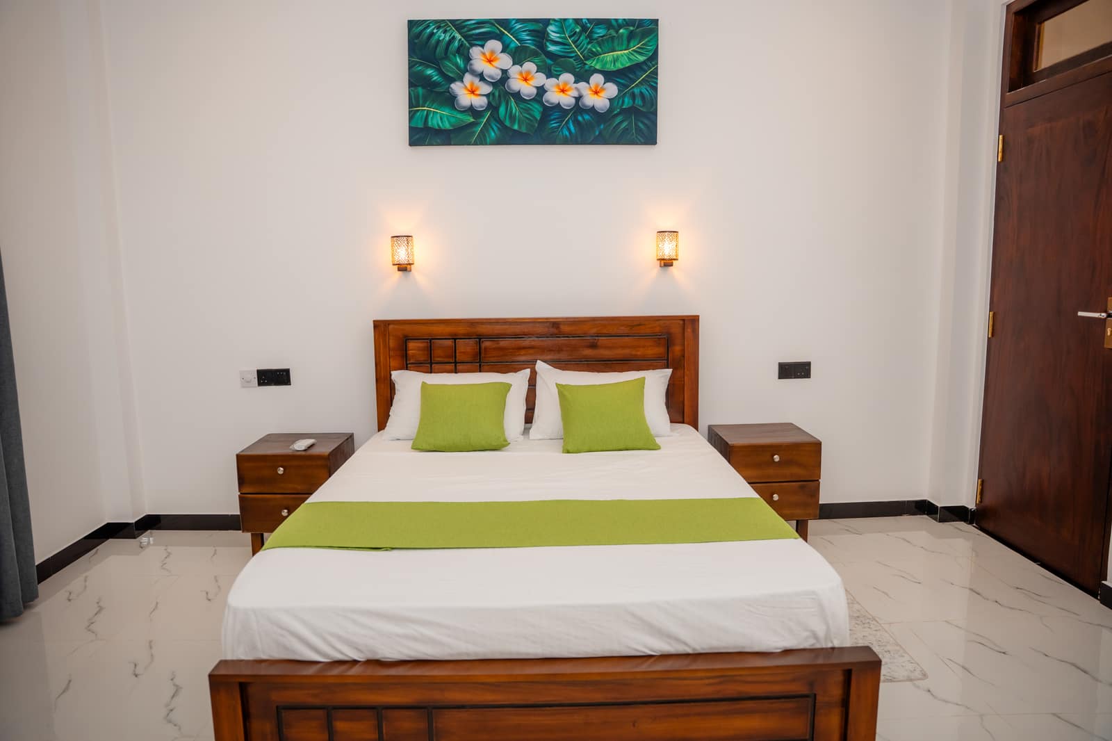 The Deluxe Queen Room, queen bed made up with green cushions beneath a framed painting
