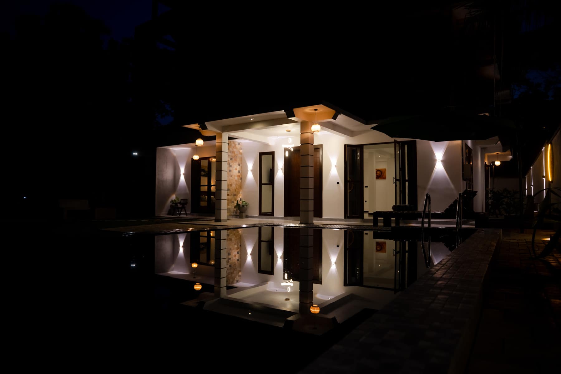 The villa lit from within at night, reflected whole in the still surface of the pool